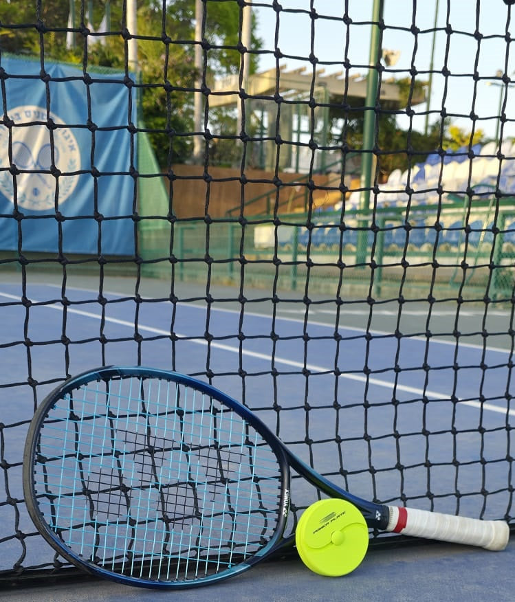 Tennis racket and power plate on a tennis court with a net in the foreground